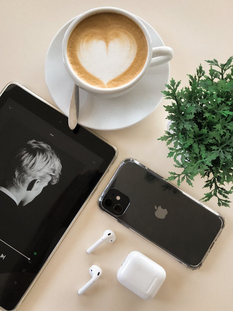 A stylish flat lay showcasing a coffee cup, gadgets, AirPods, and a plant for a modern lifestyle vibe.